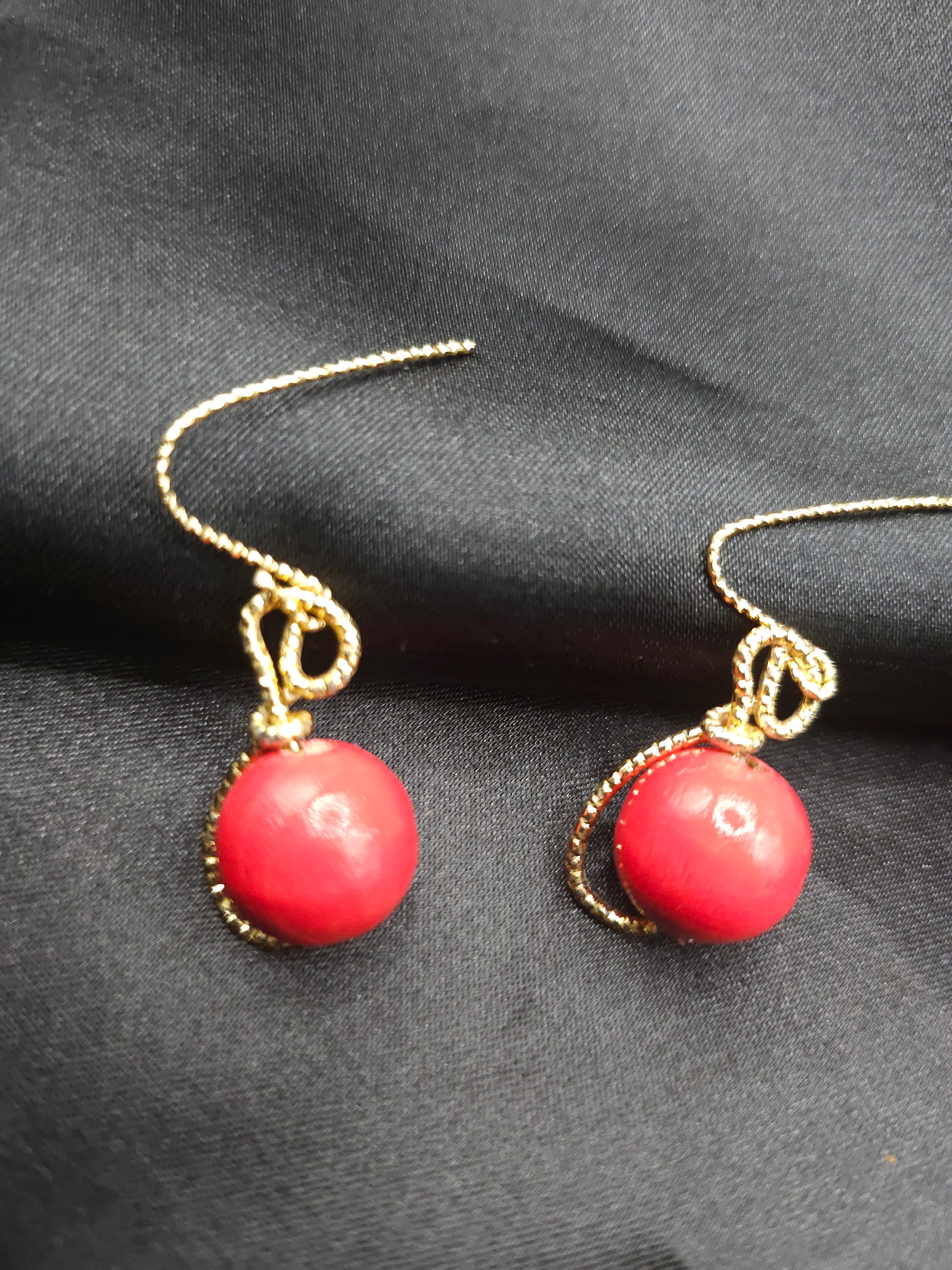 Ces petites boucles d'oreilles rondes sont entièrement modelées à la main et assemblées en France. Leurs perles en bois rouge apportent une touche de chaleur naturelle et d'authenticité à votre look. Le fil d'or (étain plaqué or 18 carats) qui entoure délicatement chaque perle crée un contraste élégant et raffiné. 